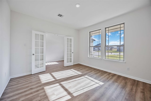 unfurnished room featuring baseboards, visible vents, wood finished floors, and french doors