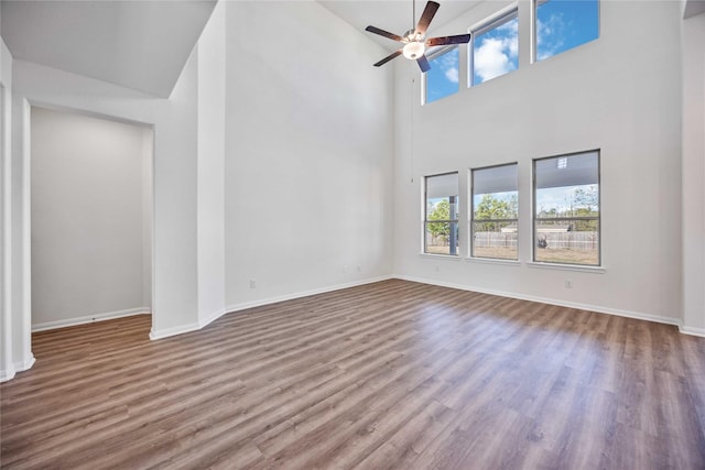 unfurnished living room featuring ceiling fan, a high ceiling, baseboards, and wood finished floors