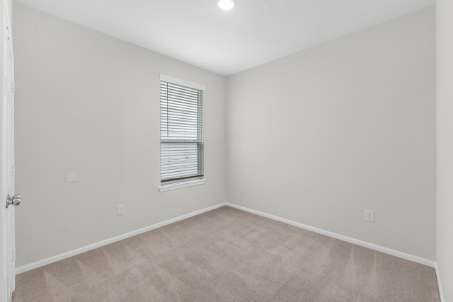 spare room featuring light carpet and baseboards