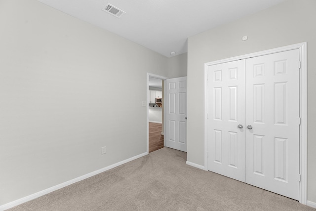 unfurnished bedroom with baseboards, visible vents, a closet, and light colored carpet