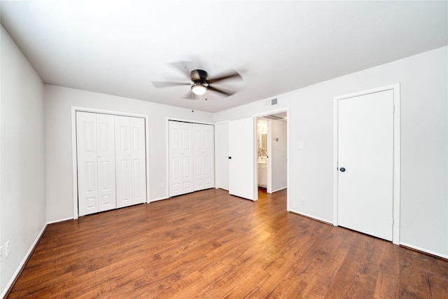 unfurnished bedroom featuring multiple closets, a ceiling fan, baseboards, and wood finished floors