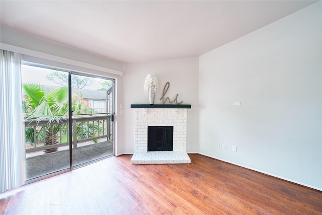 unfurnished living room featuring a brick fireplace, baseboards, and wood finished floors