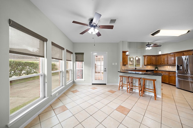 kitchen with light tile patterned floors, visible vents, stainless steel fridge with ice dispenser, tasteful backsplash, and dark countertops