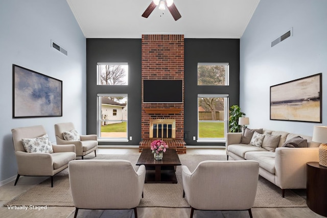 living room with a fireplace, a towering ceiling, visible vents, and crown molding