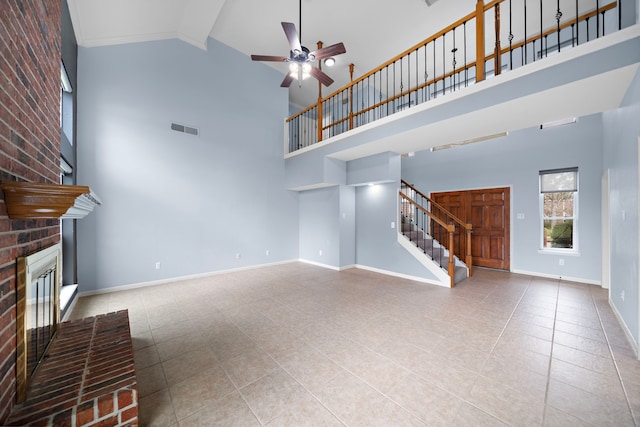 unfurnished living room with ceiling fan, visible vents, baseboards, stairway, and a brick fireplace