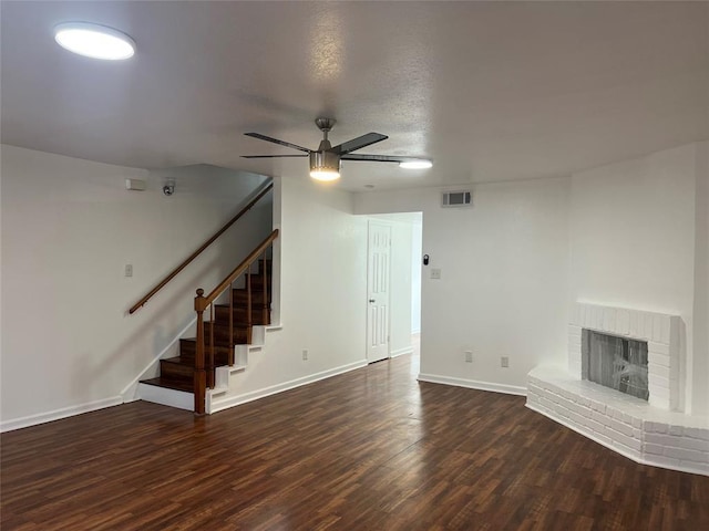 unfurnished living room with a fireplace, visible vents, a ceiling fan, wood finished floors, and stairs