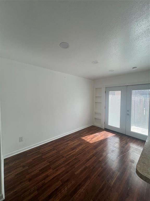 spare room featuring dark wood-style floors, built in features, french doors, a textured ceiling, and baseboards