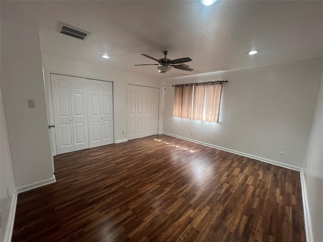 unfurnished bedroom featuring dark wood finished floors, multiple closets, recessed lighting, visible vents, and baseboards