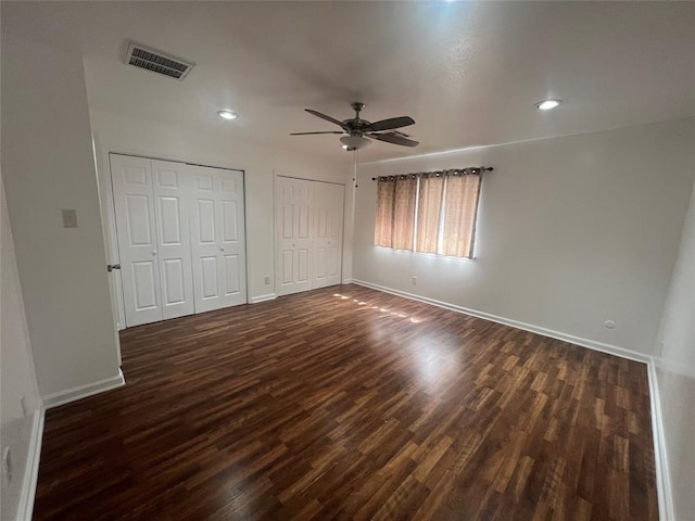 unfurnished bedroom with baseboards, dark wood finished floors, visible vents, and multiple closets