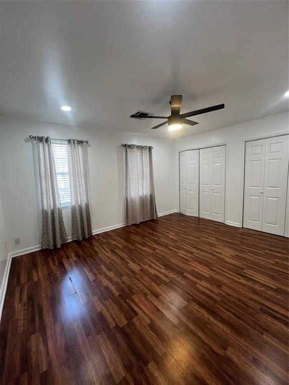 unfurnished bedroom featuring dark wood-type flooring, baseboards, and multiple closets