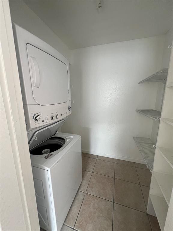 laundry room featuring light tile patterned floors, laundry area, stacked washer / dryer, and baseboards