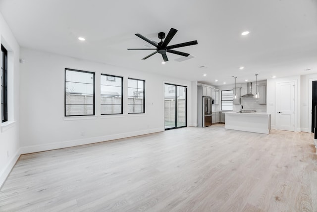 unfurnished living room with light wood-type flooring, baseboards, a sink, and recessed lighting