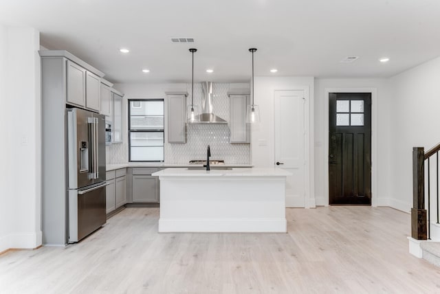 kitchen with a healthy amount of sunlight, wall chimney range hood, high quality fridge, and gray cabinets