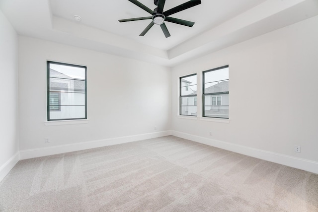 empty room featuring light carpet, a raised ceiling, a ceiling fan, and baseboards