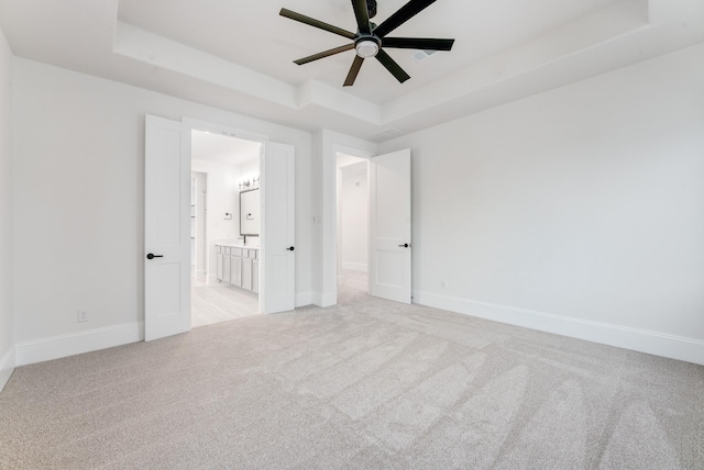 spare room featuring light carpet, baseboards, a tray ceiling, and a ceiling fan