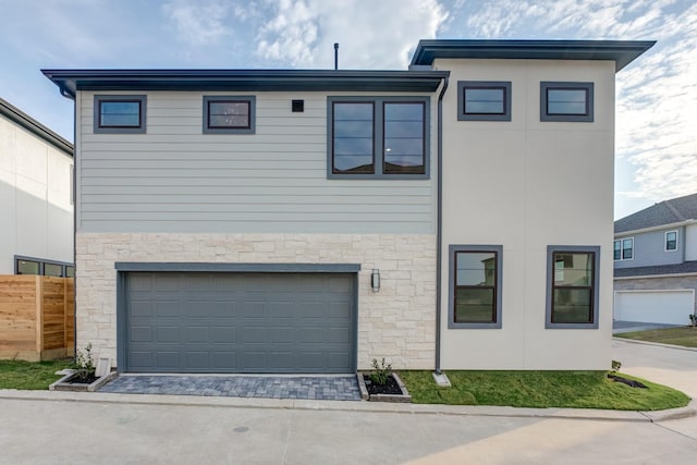 view of front of property featuring stone siding, decorative driveway, fence, and an attached garage