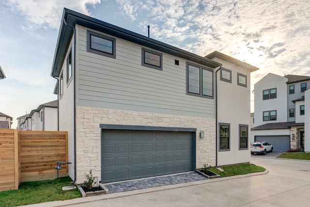 view of front of home with a garage, stone siding, fence, and driveway