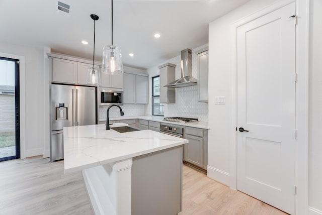 kitchen with stainless steel appliances, a sink, wall chimney range hood, and gray cabinetry