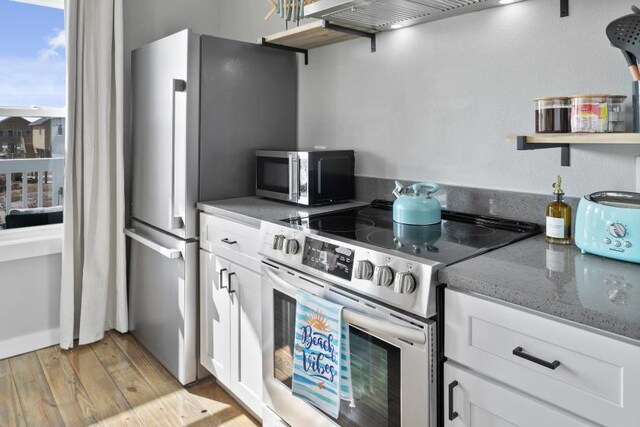 kitchen featuring light wood finished floors, white cabinets, dark stone counters, appliances with stainless steel finishes, and open shelves