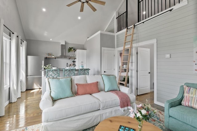 living area featuring a ceiling fan, light wood-style flooring, wood walls, high vaulted ceiling, and recessed lighting