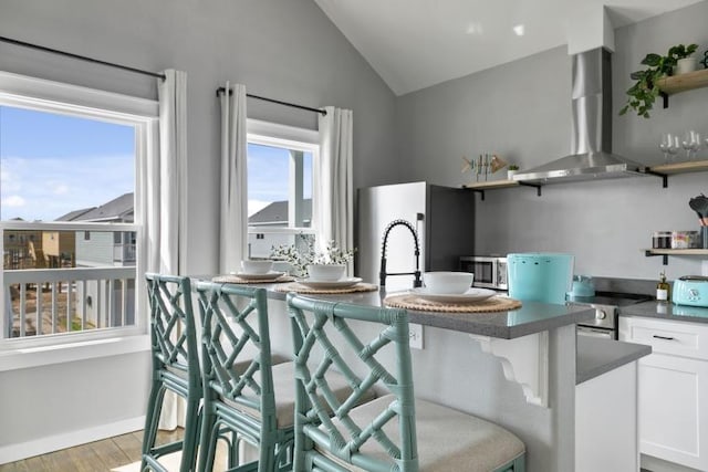 kitchen with open shelves, stainless steel appliances, dark countertops, lofted ceiling, and wall chimney range hood