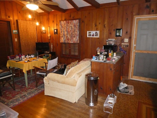 living area featuring a ceiling fan, beam ceiling, wood walls, and wood finished floors