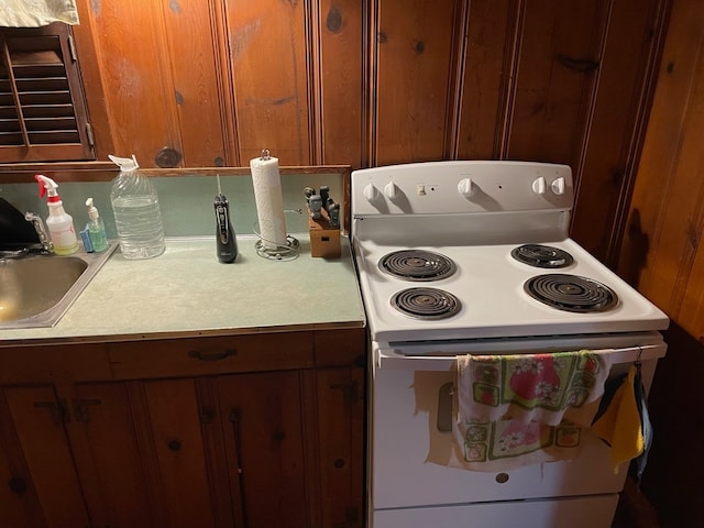 kitchen with brown cabinets, light countertops, a sink, and white electric range oven