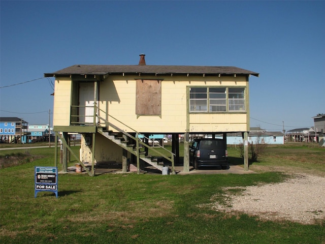 rear view of house with stairs, a carport, a lawn, and roof with shingles