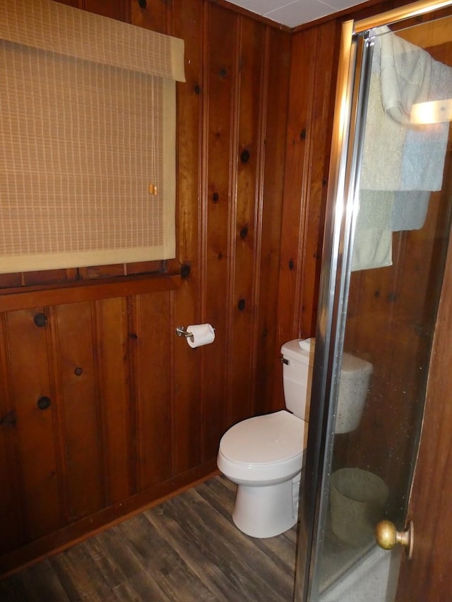 full bath featuring toilet, a shower stall, wooden walls, and wood finished floors