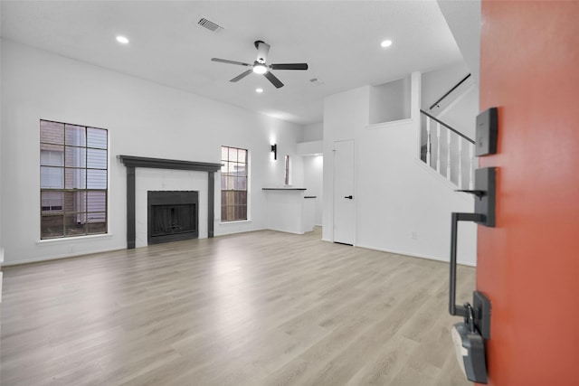 unfurnished living room with a tile fireplace, visible vents, a ceiling fan, stairs, and light wood-type flooring