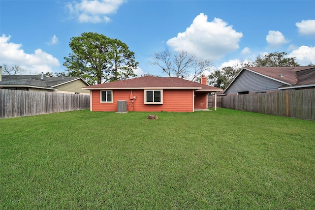 back of property with central AC unit, a lawn, a chimney, and a fenced backyard