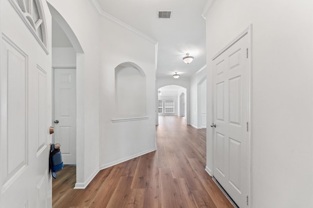 hall with arched walkways, crown molding, and wood finished floors