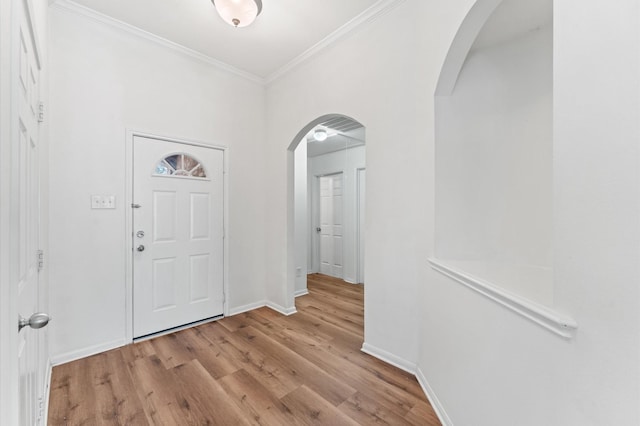 entrance foyer featuring arched walkways, ornamental molding, wood finished floors, and baseboards