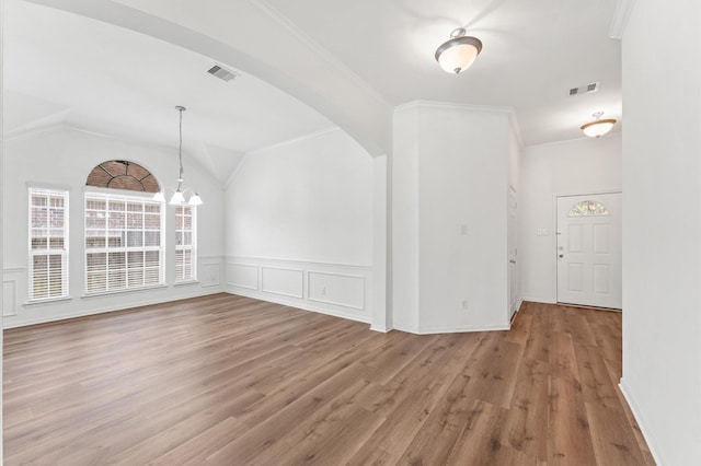 spare room featuring vaulted ceiling, arched walkways, wood finished floors, and visible vents