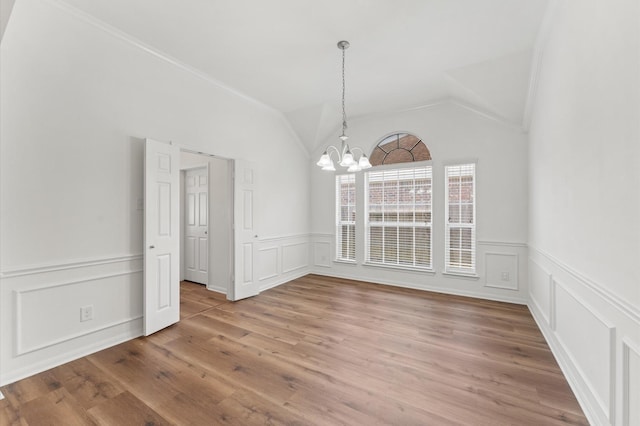 unfurnished dining area with a chandelier, vaulted ceiling, light wood-style flooring, and a decorative wall