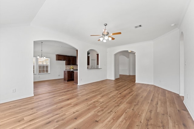 unfurnished living room with arched walkways, ceiling fan with notable chandelier, visible vents, light wood finished floors, and crown molding