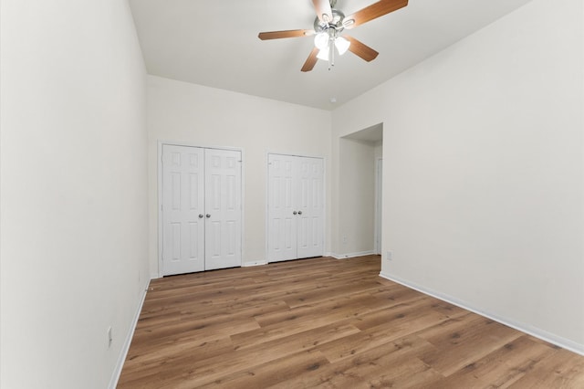 unfurnished bedroom with multiple closets, light wood-type flooring, baseboards, and a ceiling fan