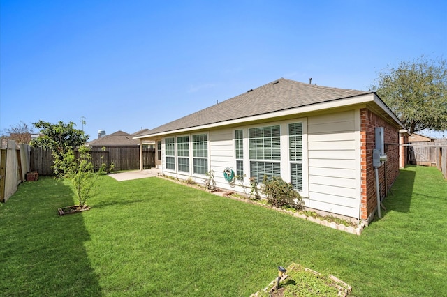 rear view of property featuring a shingled roof, brick siding, a lawn, and a fenced backyard