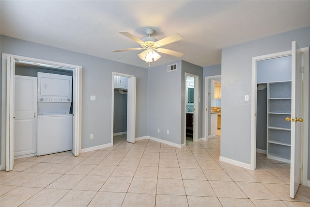 unfurnished bedroom with two closets, light tile patterned floors, visible vents, stacked washing maching and dryer, and baseboards