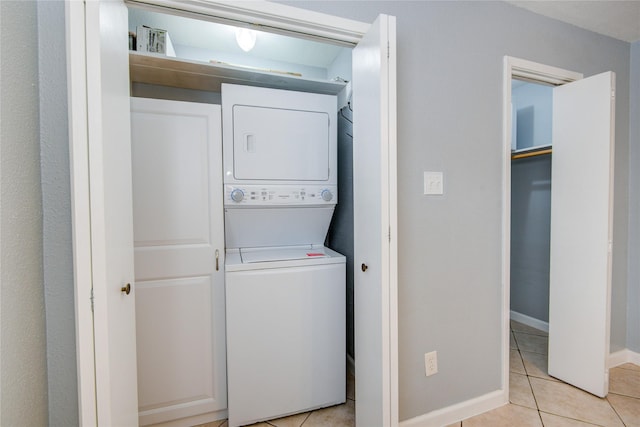 laundry room featuring light tile patterned floors, laundry area, stacked washer / dryer, and baseboards