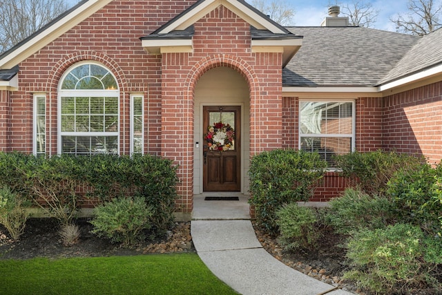 property entrance featuring a shingled roof, a chimney, and brick siding