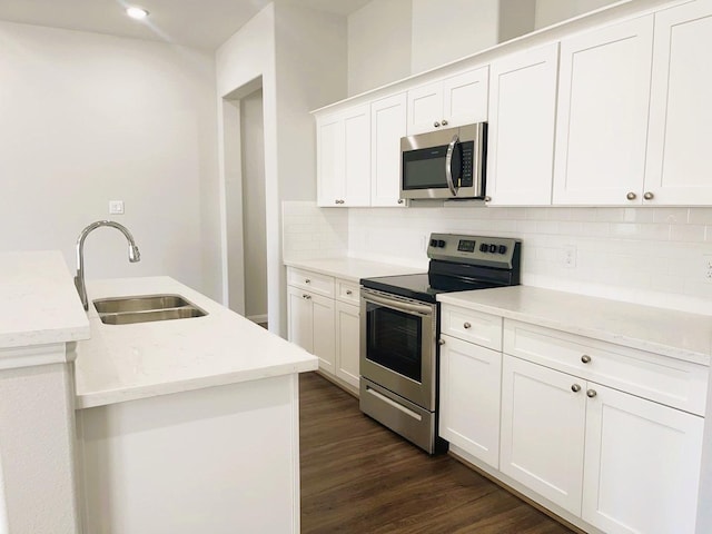 kitchen with dark wood-type flooring, a sink, stainless steel appliances, white cabinetry, and backsplash