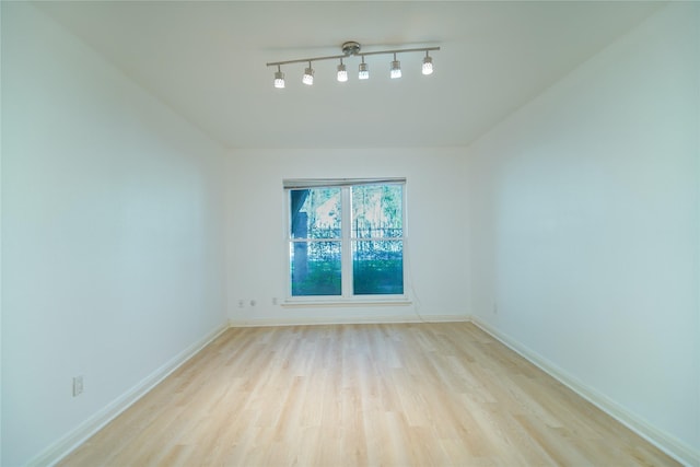 spare room featuring light wood-type flooring, rail lighting, and baseboards