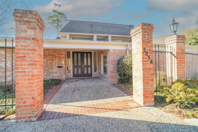 property entrance with a shingled roof, fence, and brick siding