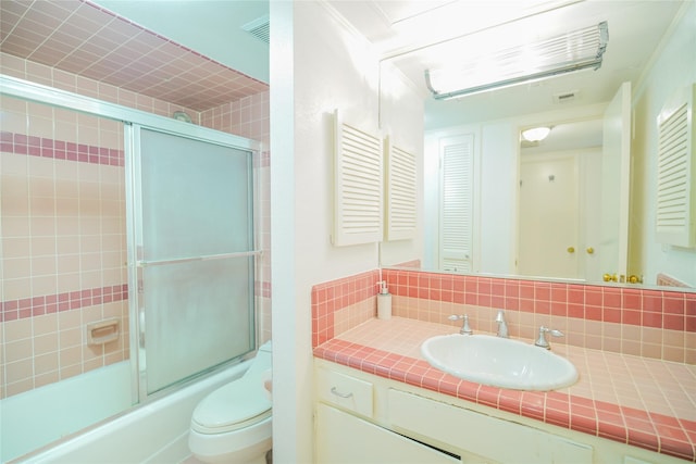 bathroom featuring visible vents, bath / shower combo with glass door, toilet, vanity, and backsplash