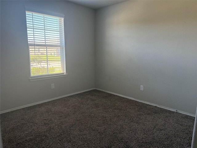 spare room featuring baseboards and dark carpet