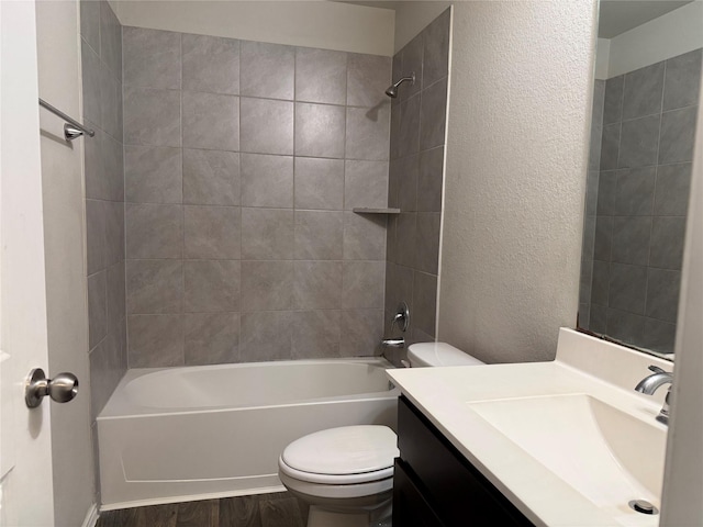 bathroom with a textured wall, toilet, wood finished floors, vanity, and shower / washtub combination