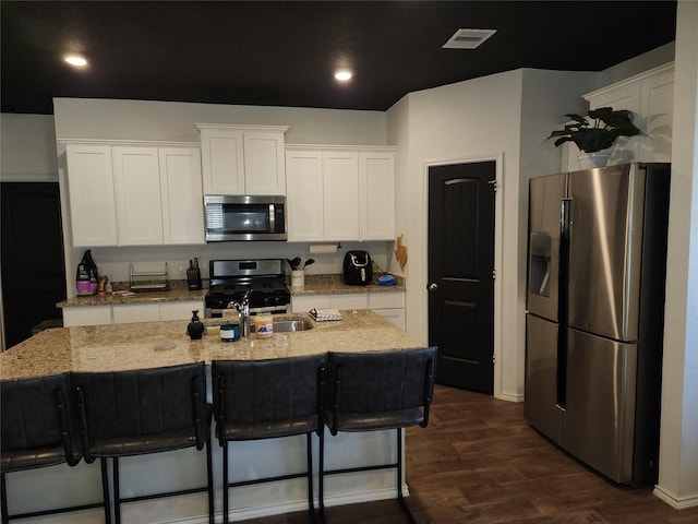 kitchen featuring a center island with sink, visible vents, dark wood-style flooring, stainless steel appliances, and white cabinetry