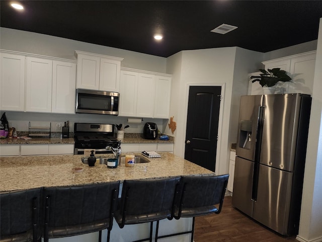 kitchen featuring visible vents, white cabinets, light stone counters, appliances with stainless steel finishes, and dark wood-type flooring