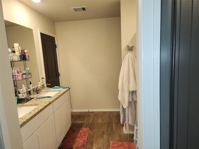 bathroom with a sink, wood finished floors, visible vents, baseboards, and double vanity